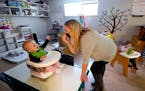 FILE - Amy McCoy signs to a baby about food as a toddler finishes lunch behind at her Forever Young Daycare facility, Monday, Oct. 25, 2021, in Mountl