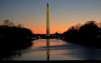 The Washington Monument is seen at a distance as a jogger trots near the Lincoln Memorial Reflecting Pool before sunrise on Capitol Hill in Washington