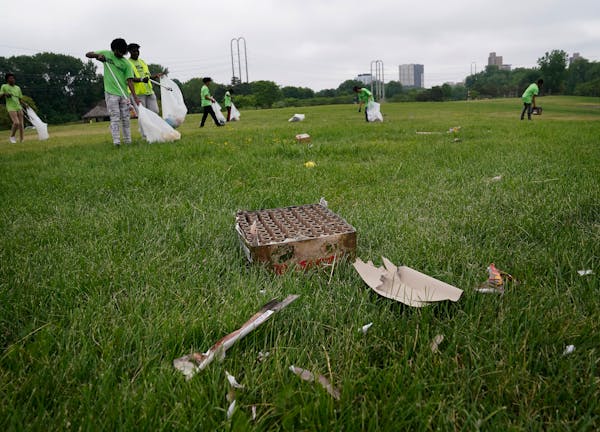 Spent fireworks cases litter the ground on Boom Island Park as workers from Teen Teamworks, a summer employment program, pick up litter in the park Tu