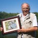 Chuck Delaney, owner and promoter of Game Fair, last week posed for a portrait with a photo of his wife Loral I, on the Game Fair grounds in Ramsey, M