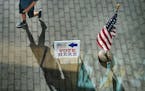 A man casts a shadow while walking by a voting sign at the Minneapolis Central Library during the primary election that includes the 5th congressional