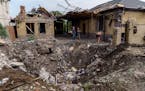Debris is cleared next to a crater caused by a rocket strike on a house in Kramatorsk, Donetsk region, eastern Ukraine, Friday, Aug. 12, 2022. There w
