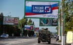FILE - A military vehicle drives along a street with a billboard that reads: “With Russia forever, September 27”, prior to a referendum in Luhansk
