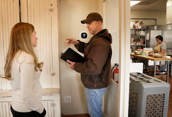 Center for Energy & Environment (CEE) HVAC consultant Taylor Smith sets a programable thermostat, explaining how the device works to Erin Bailey, who 