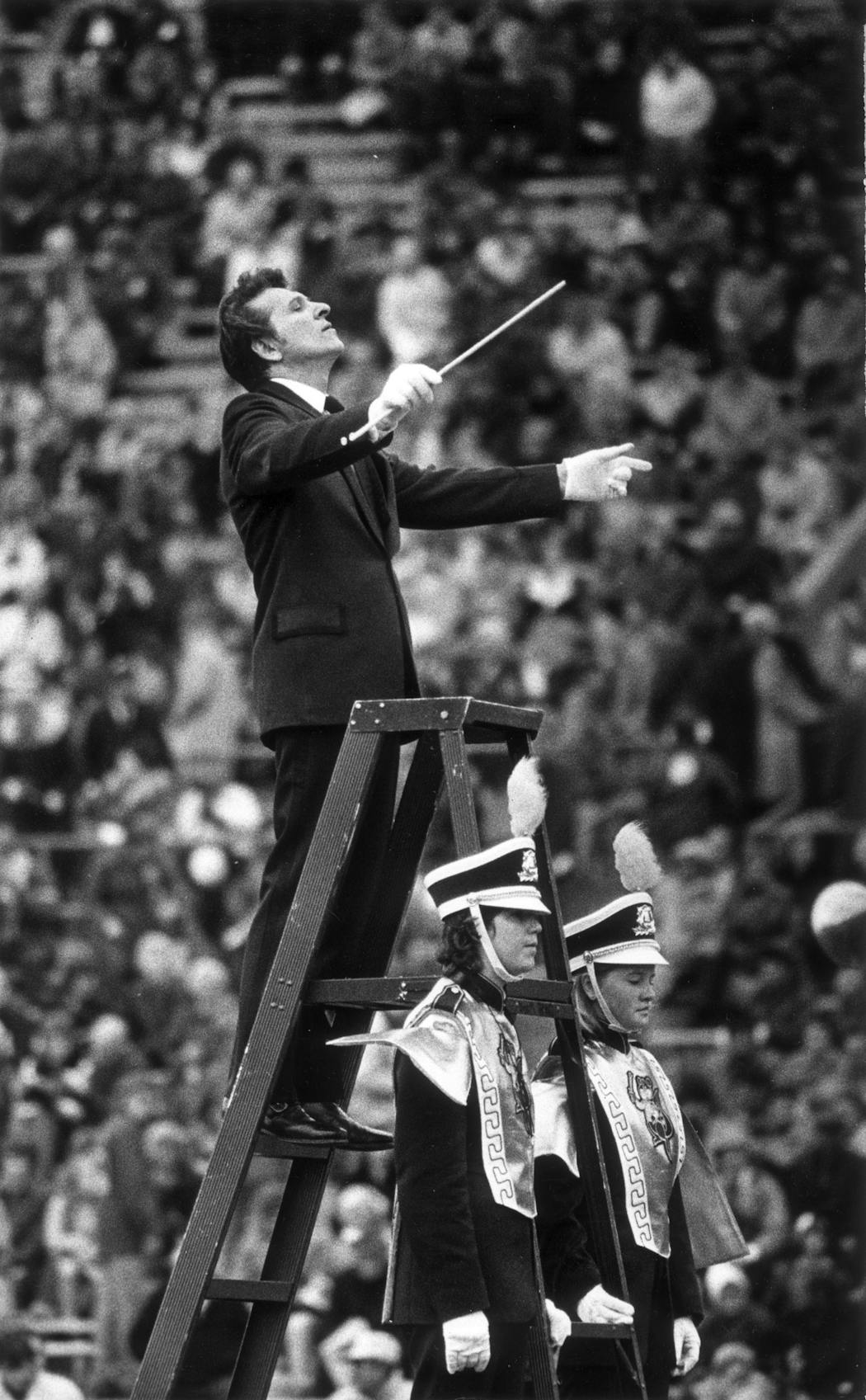 Dr. Frank Bencriscutto, known as “Dr. Ben,” conducted the marching band circa 1973, not long after it started to include women members. Note one man and one woman are flanking the ladder-podium in this photo.