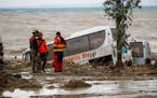 Rescuers stood next to a bus carried away after heavy rainfall triggered landslides that collapsed buildings and left as many as 12 people missing, in