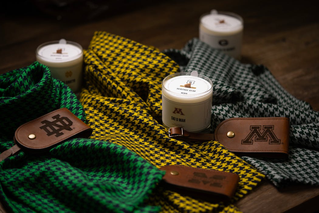 A selection of scarves, leather luggage tags, and scented candles branded with college logos and colorways, photographed in the Heritage Gear warehouse in Edina, Minn. 