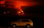 A man talks on a phone in his car alongside Saddle Road as the Mauna Loa volcano erupts Wednesday, Nov. 30, 2022, near Hilo, Hawaii. Hundreds of peopl