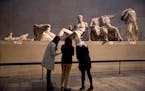 Women stand by a marble statue of a naked youth thought to represent Greek god Dionysos, center, from the east pediment of the Parthenon, on display d