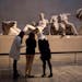 Women stand by a marble statue of a naked youth thought to represent Greek god Dionysos, center, from the east pediment of the Parthenon, on display d