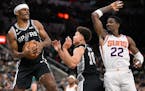 San Antonio Spurs’ Alize Johnson, left, grabs the rebound ahead of Phoenix Suns’ Deandre Ayton (22) and Spurs forward Isaiah Roby during the first