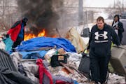 A tent catches fire as volunteers, workers and residents take down and clean up a homeless encampment Wednesday in the Cedar-Riverside neighborhood in