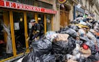 A cyclist rides past an uncollected garbage pile next to the cafe “The President” in Paris, Tuesday, March 21, 2023. The bill pushed through by Pr