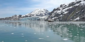 A Glacier Bay National Park tour boat plies the waters of the Glacier Bay channel near the largest glacier in the area, Margerie Glacier, showing the 