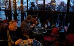 People enjoy a meal or drink as riot police officers stand outside after a demonstration Tuesday, March 28, 2023 in Paris. It’s the latest round of 