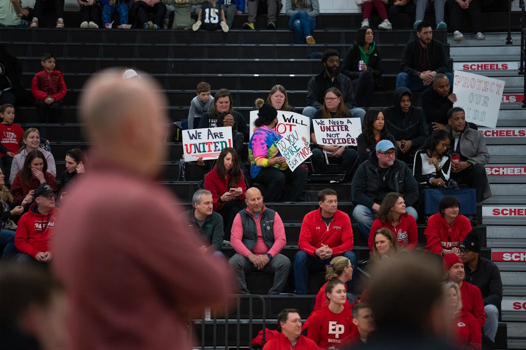 Eden Prairie’s David Flom coached from the sideline, foreground, while people in the stands held signs protesting his reinstatement.