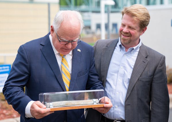 Gov. Tim Walz is presented with an old lead pipe in a glass box by Paul Austin, executive director of Conservation Minnesota, after a bill signing cer