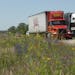 Semitrailer trucks on I-80 in western Iowa with wildflowers.