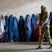 FILE - A Taliban fighter stands guard as women wait to receive food rations distributed by a humanitarian aid group, in Kabul, Afghanistan, Tuesday, M