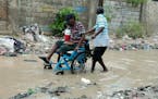 A man in a wheelchair is helped to make his way through a flooded street after a heavy rain, in Port-au-Prince, Haiti, Saturday, June 3, 2023. 