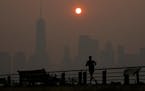 A man runs in front of the sun rising over the lower Manhattan skyline in Jersey City, N.J., Thursday, June 8, 2023. Intense Canadian wildfires are bl
