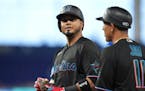 Miami Marlins’ Luis Arraez, left, looks toward the stands as he listens to first base coach Jon Jay (11) following a base hit against the Kansas Cit