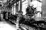 A worker at the St. Paul Ford Plant guides an engine down into a vehicle frame in 1955.
