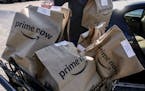 Amazon Prime Now bags full of groceries are loaded for delivery by a part-time worker outside a Whole Foods store in 2018, in Cincinnati.